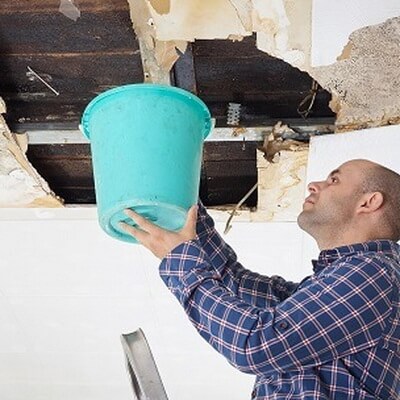 man holding a bucket to ceiling to catch water leak